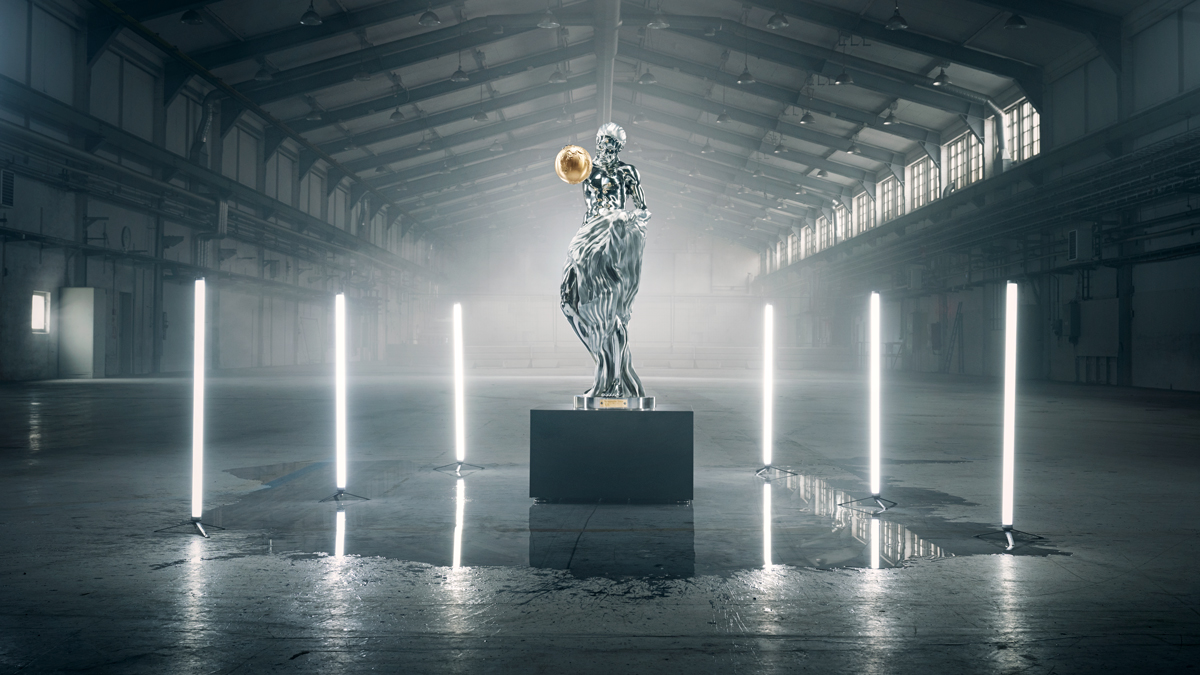 A steel statue of a woman holding a round gold-colored ball on one of her hands.